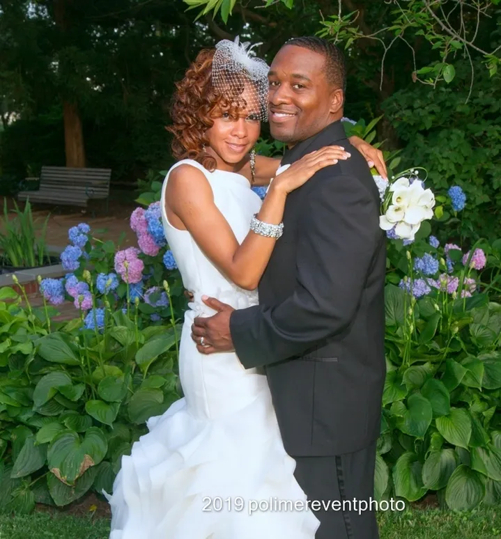 A man and woman posing for a picture in front of flowers.