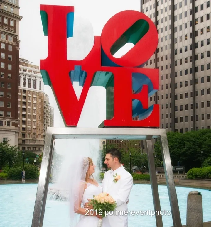 A bride and groom standing in front of the love sign.